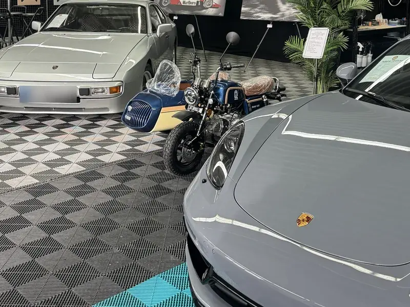 Showroom mit Sportwagen und Motorrad auf Schachbrett-Klickfliesen in Schwarz und Hellgrau mit türkisen Akzenten